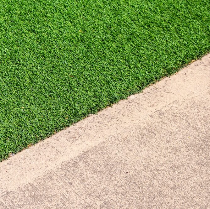 Eco-friendly green artificial synthetic grass next to a clean concrete sidewalk. Close up.